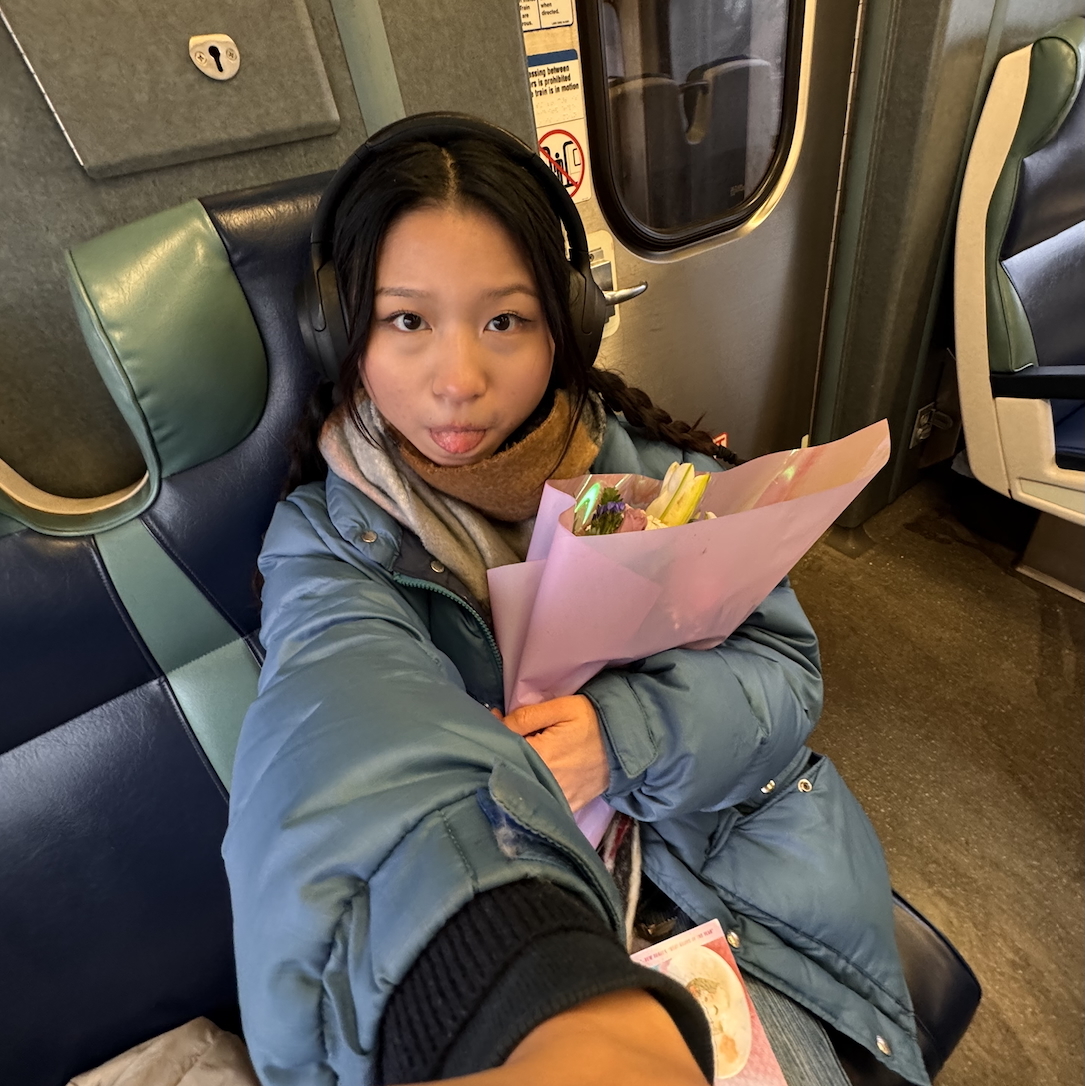 A selfie of a girl on a train, holding flowers.