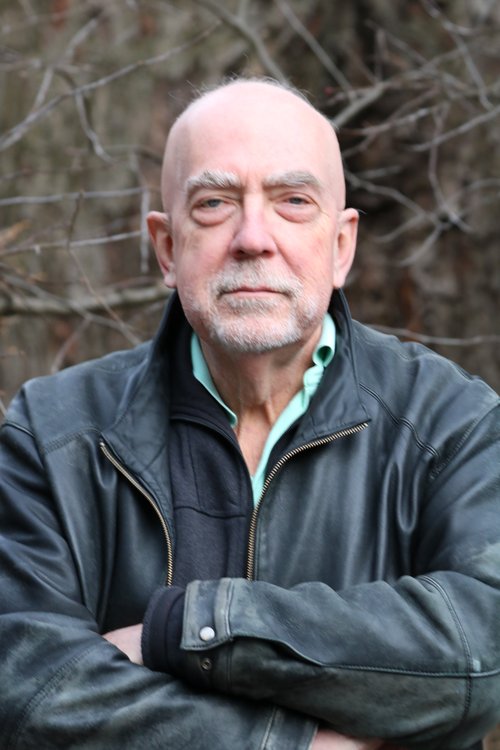 A photo of Maurice smiling with his arms crossed.